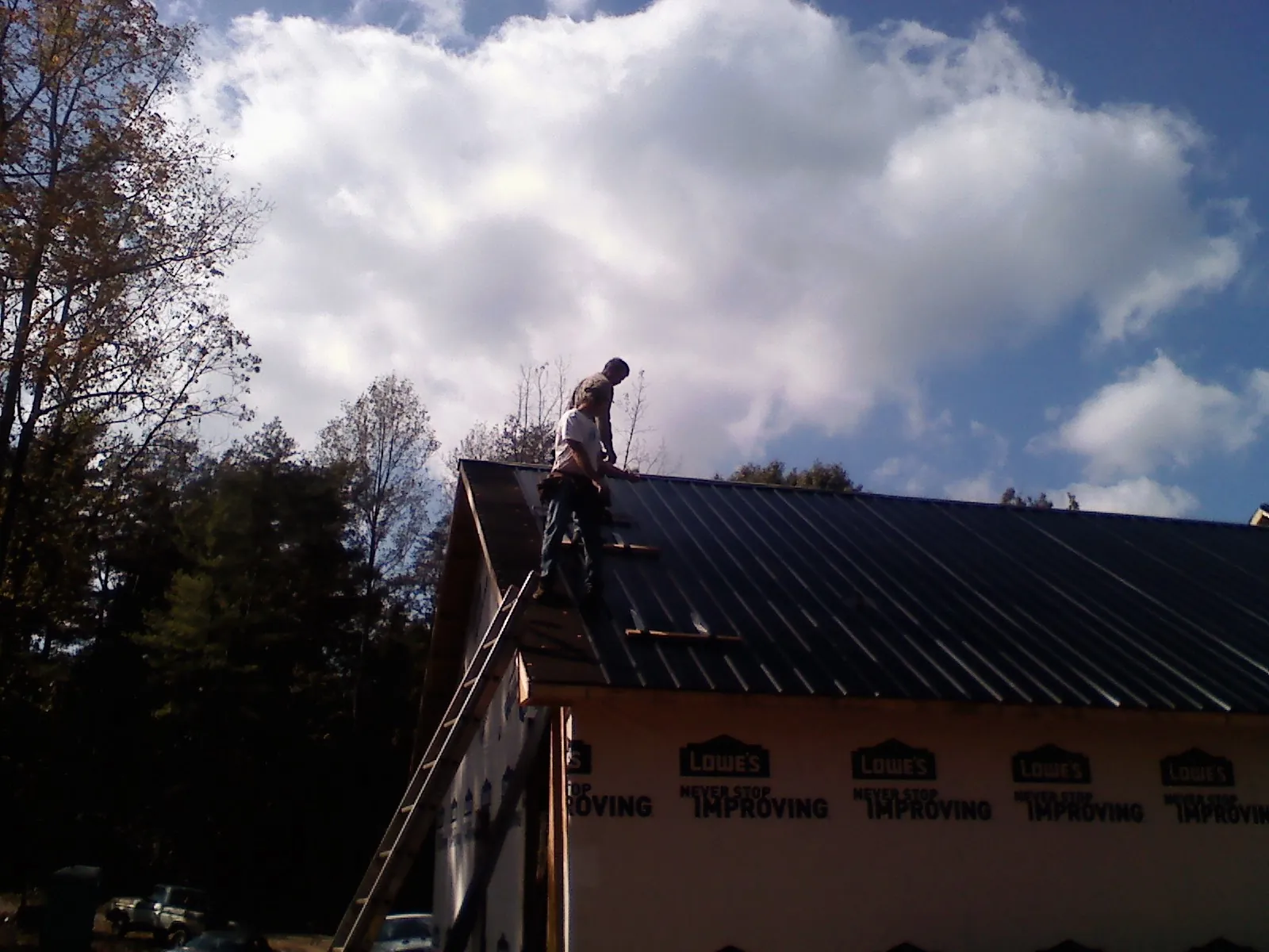 Roofer fastening dark metal panels high against a cloudy sky, from a Roof Inspection job in Snohomish