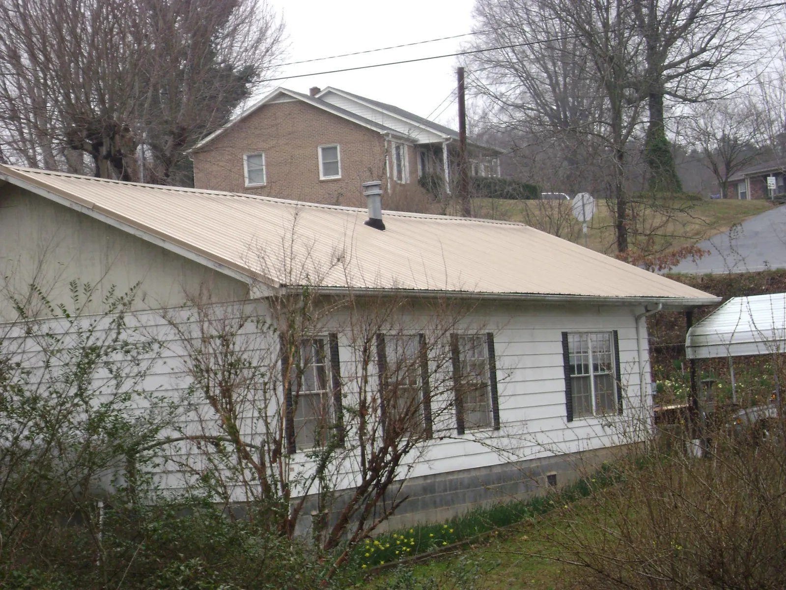 Tan metal roof on a white sided house set into a hillside — Commercial Roofing by Roofing Brothers in Snohomish